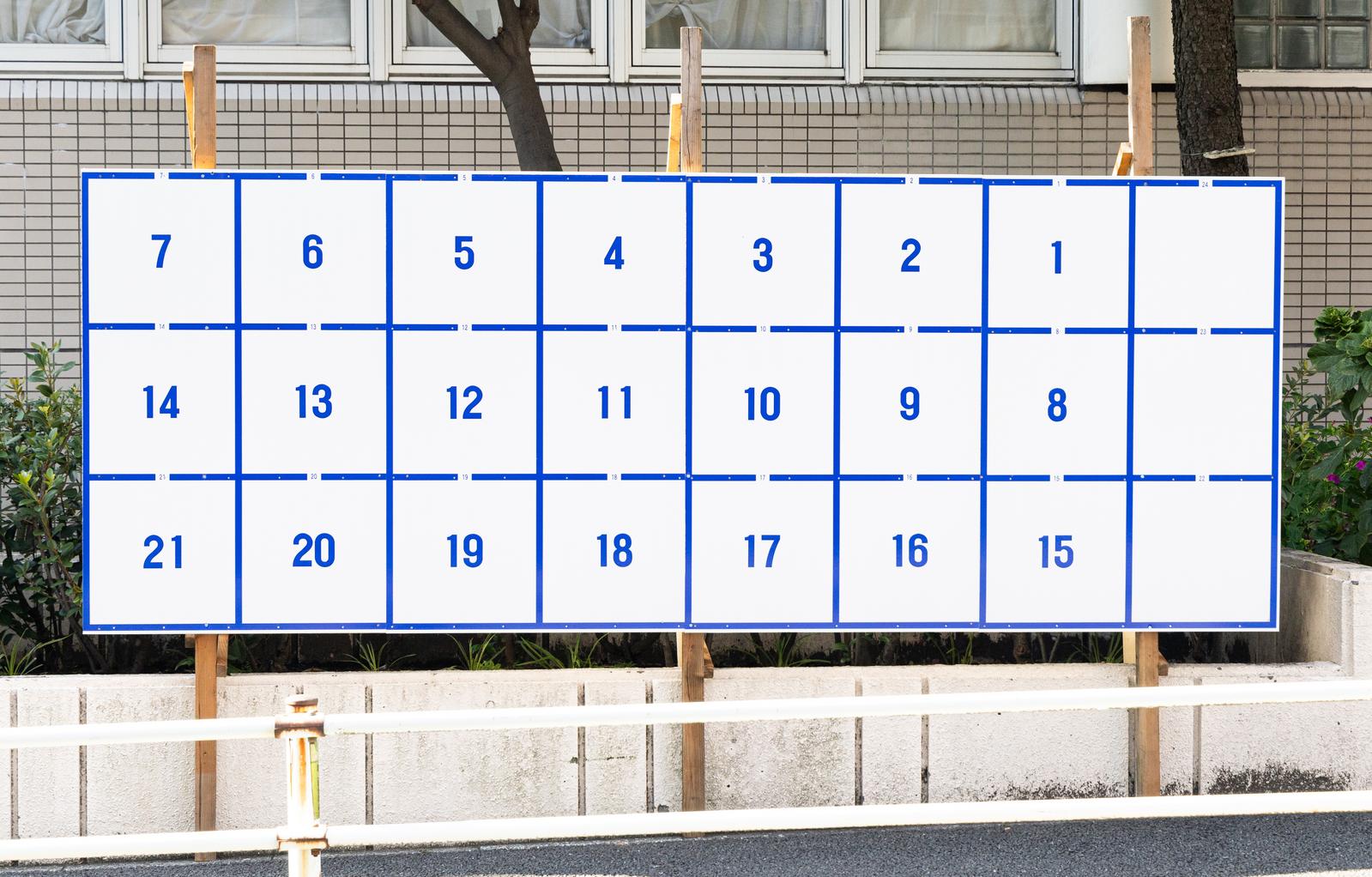 1番から21番までの番号が表示された選挙掲示板にポスターが貼られている