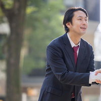 支援者と握手を交わす紺のスーツ姿の男性政治家の写真