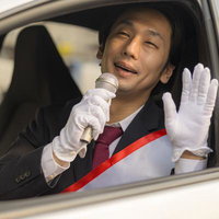 自動車の窓から身を乗り出してマイクで演説する選挙活動中の男性の写真