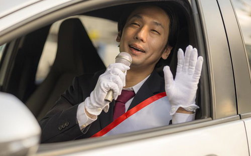 自動車の窓から身を乗り出してマイクで演説する選挙活動中の男性