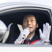 車窓からマイクを持って手を振る選挙人の政治活動の写真