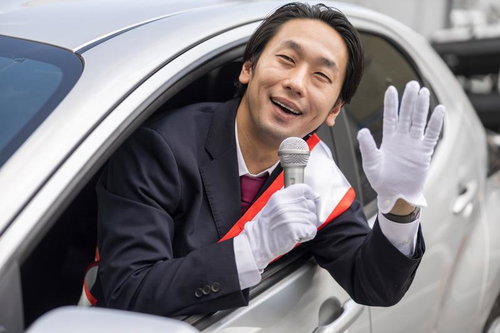 停車中の白い車から身を乗り出してマイクで演説する男性政治家