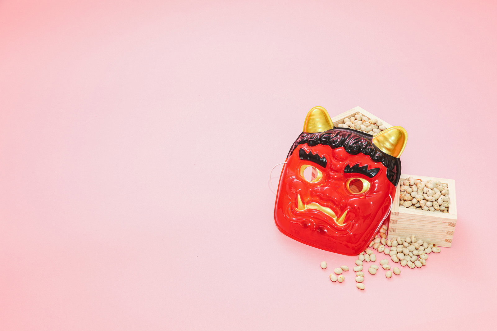 ピンクの背景に赤い鬼の面と升に入った節分の豆が置かれている