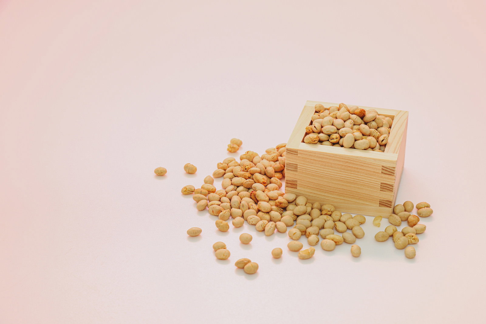 木製の枡から溢れ出る節分用の大豆がピンク背景に配置された写真