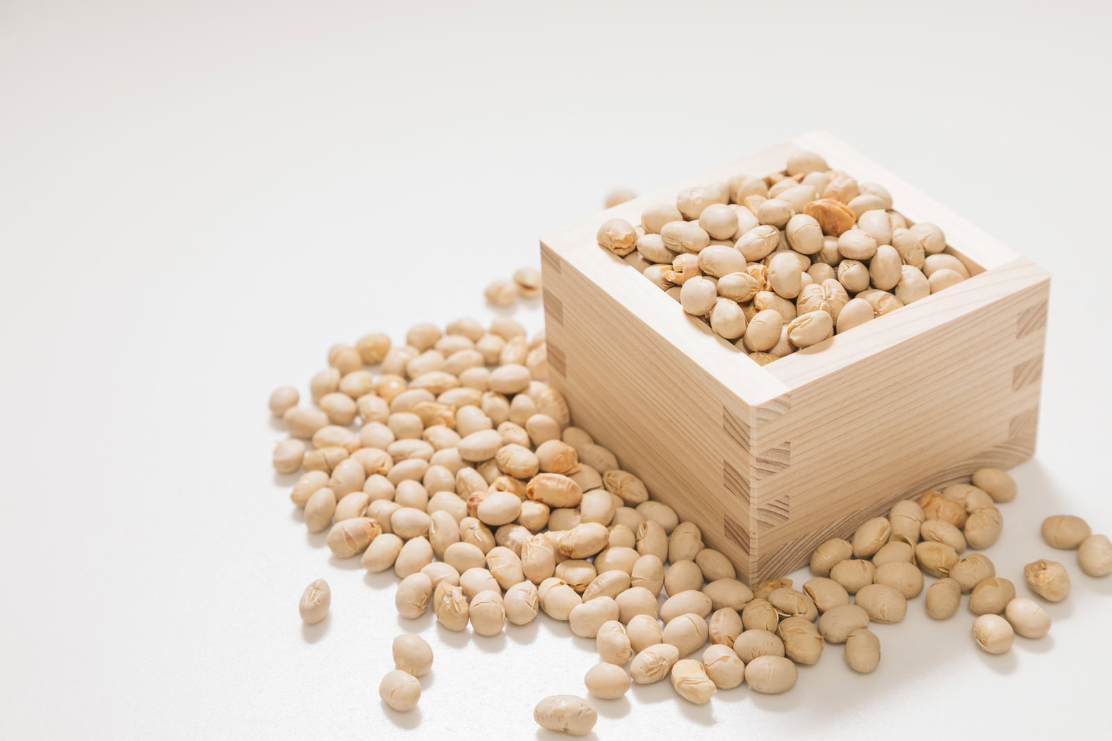 白い枡に入った節分の大豆と周囲に散らばる豆