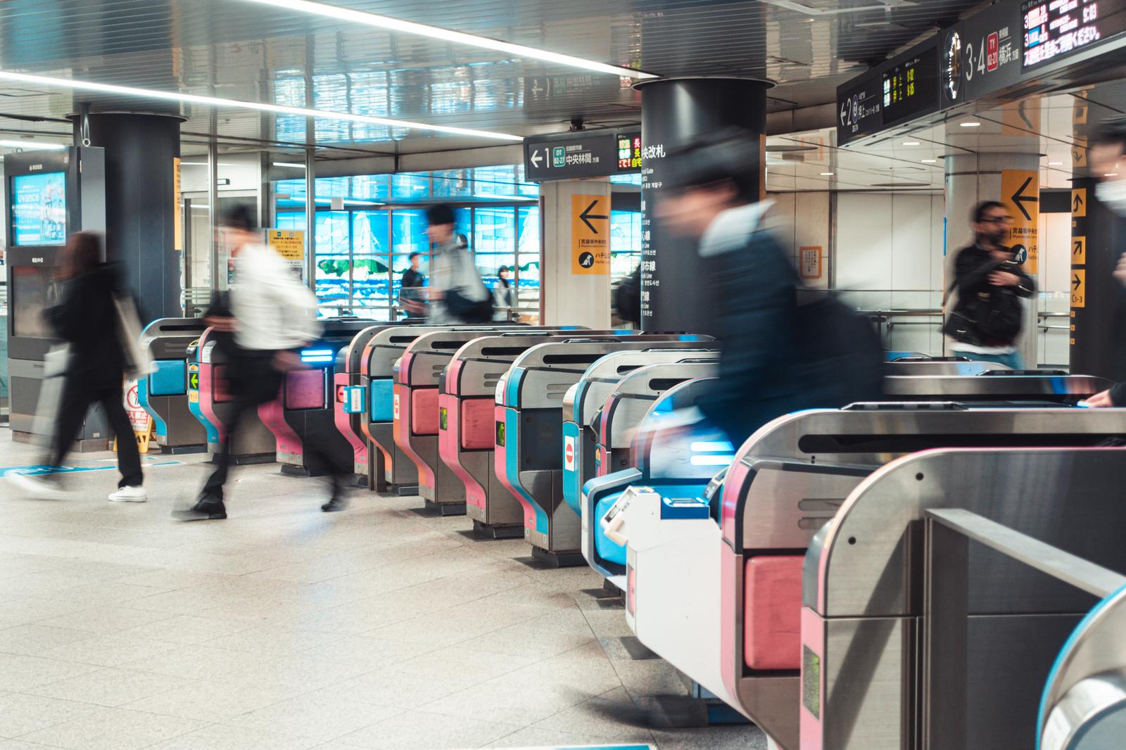 渋谷駅の地下鉄改札を通る通勤客たち。ピンクと水色の改札機が複数並んでいる