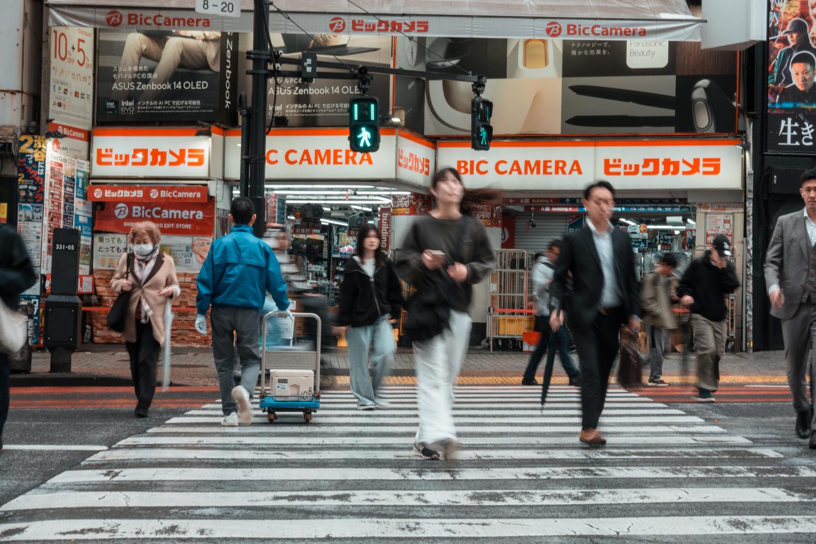 Multiple pedestrians walking across the crosswalk in front of Bic Camera in Shibuya