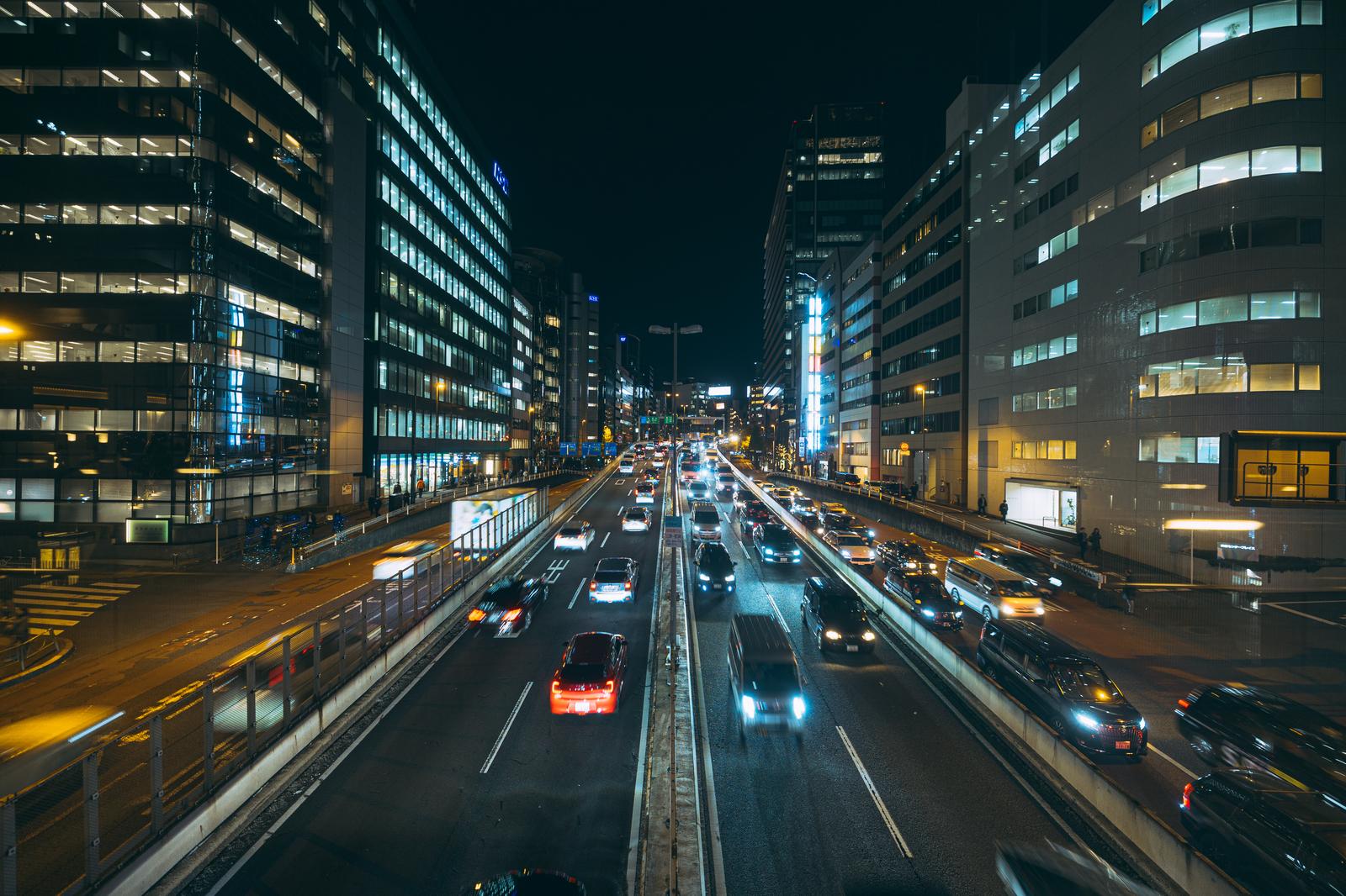 夜間の首都高を走行する多数の車と両側のオフィスビル群