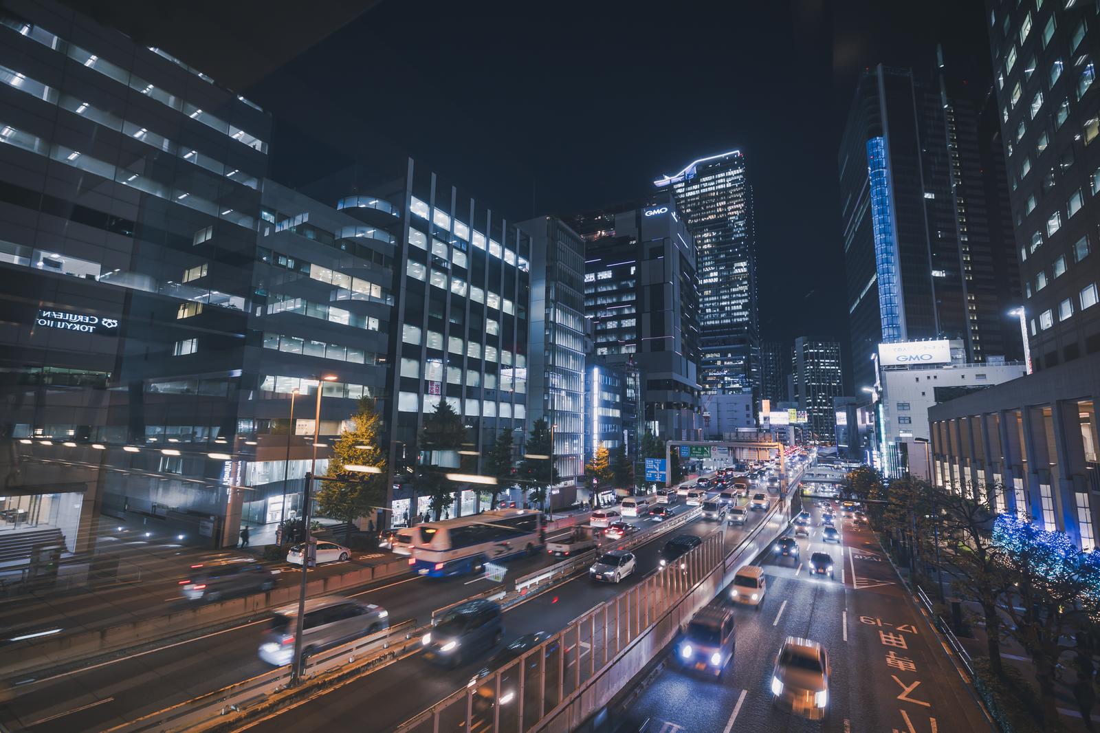夜間に照明で輝く高層ビル群と走行車のライトが見える渋谷の夜景