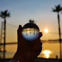 手に持ったヤシの木と夕日が映り込む水晶玉の写真