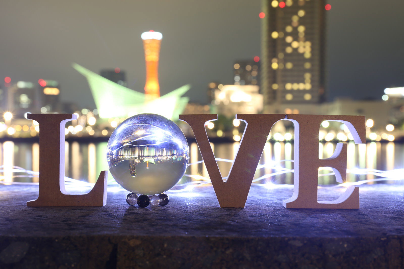 ライトアップされた夜景を背景に、LOVEの文字オブジェクトと透明な水晶玉が並んでいる