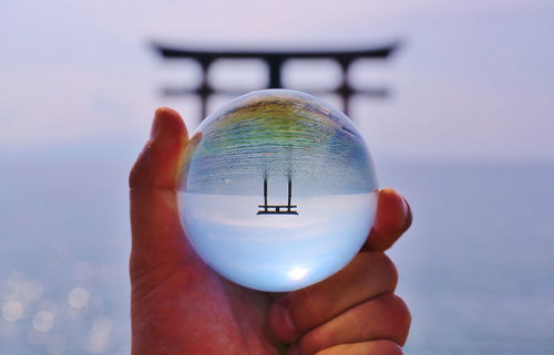 手に持った水晶玉に逆さに映り込む海上の鳥居
