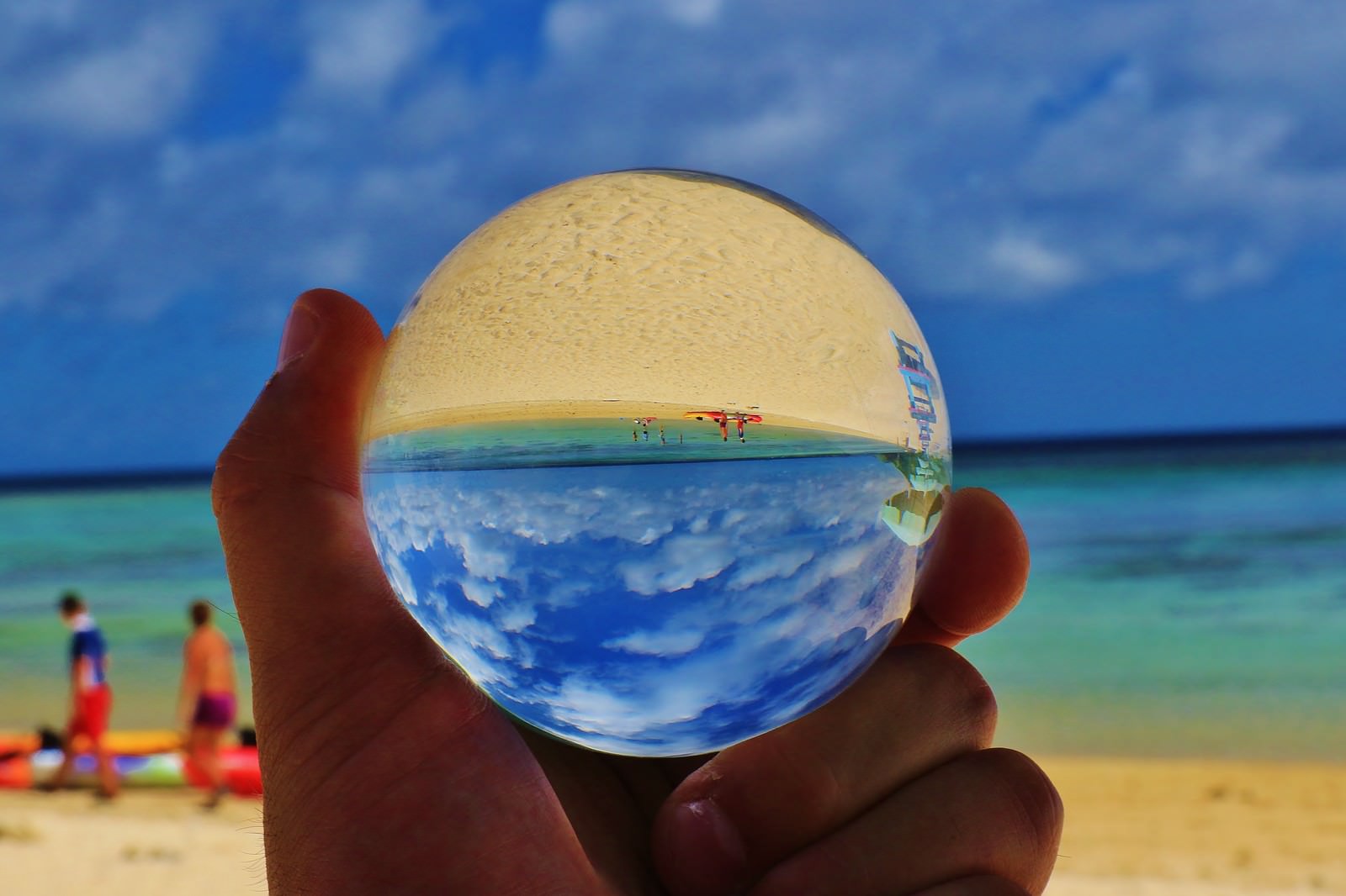 真夏のビーチで水晶玉を手に持つ様子、球体に海と青空が映る
