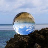海岸の岩場に置かれた水晶玉に映りこむ海と空の写真