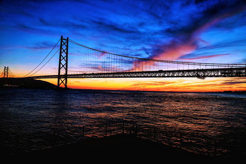 朝焼けに染まる海の吊橋のシルエット、夜明け前の空と海岸線