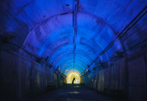 青い照明のアーチ型トンネルと出口の光に向かう人影