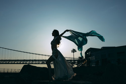 夕暮れの海岸で布をはためかせながら踊る女性のシルエット