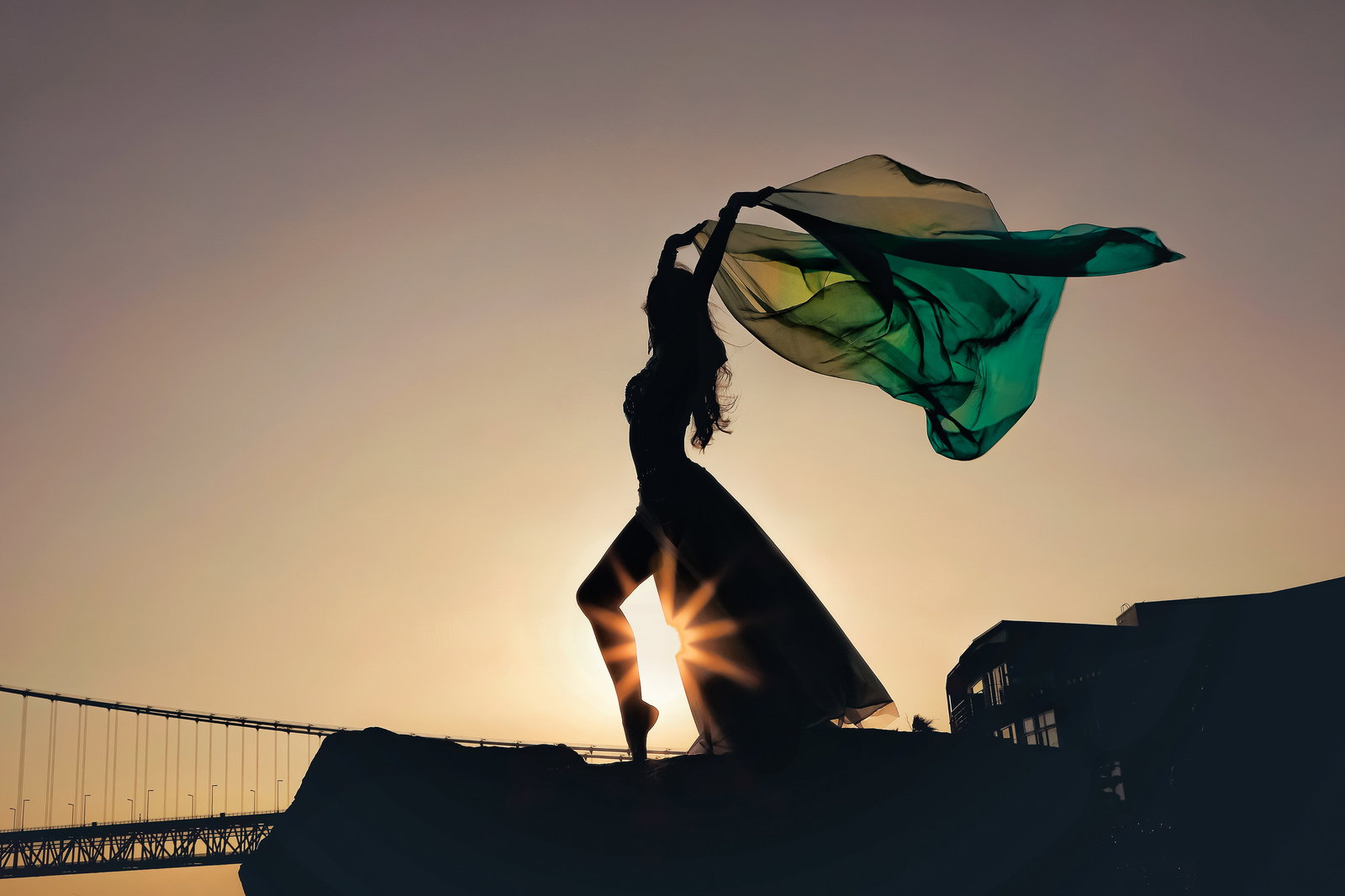 Silhouette of a female dancer performing with billowing green cloth backlit by the sunset