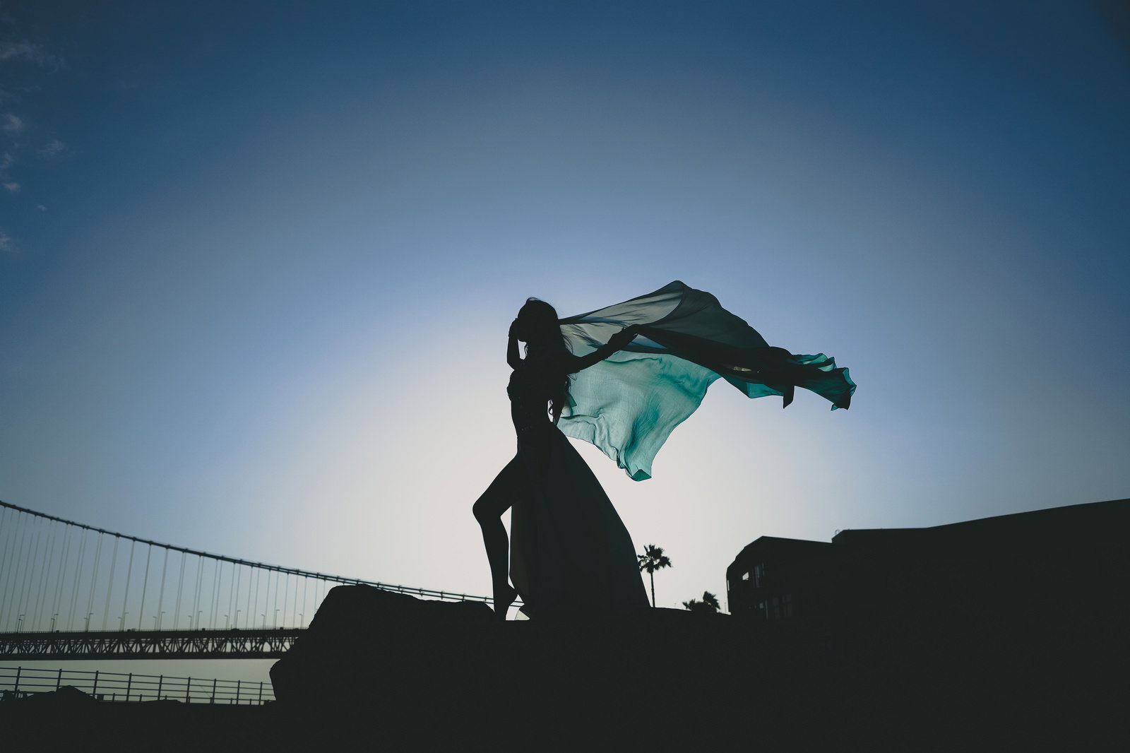 夕暮れの空を背景に布をはためかせて踊る女性のシルエット［モデル：モデルリリース］