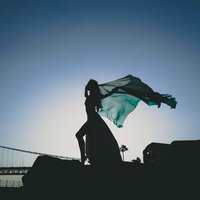 日没に布をはためかせて舞う踊り子のシルエットの写真