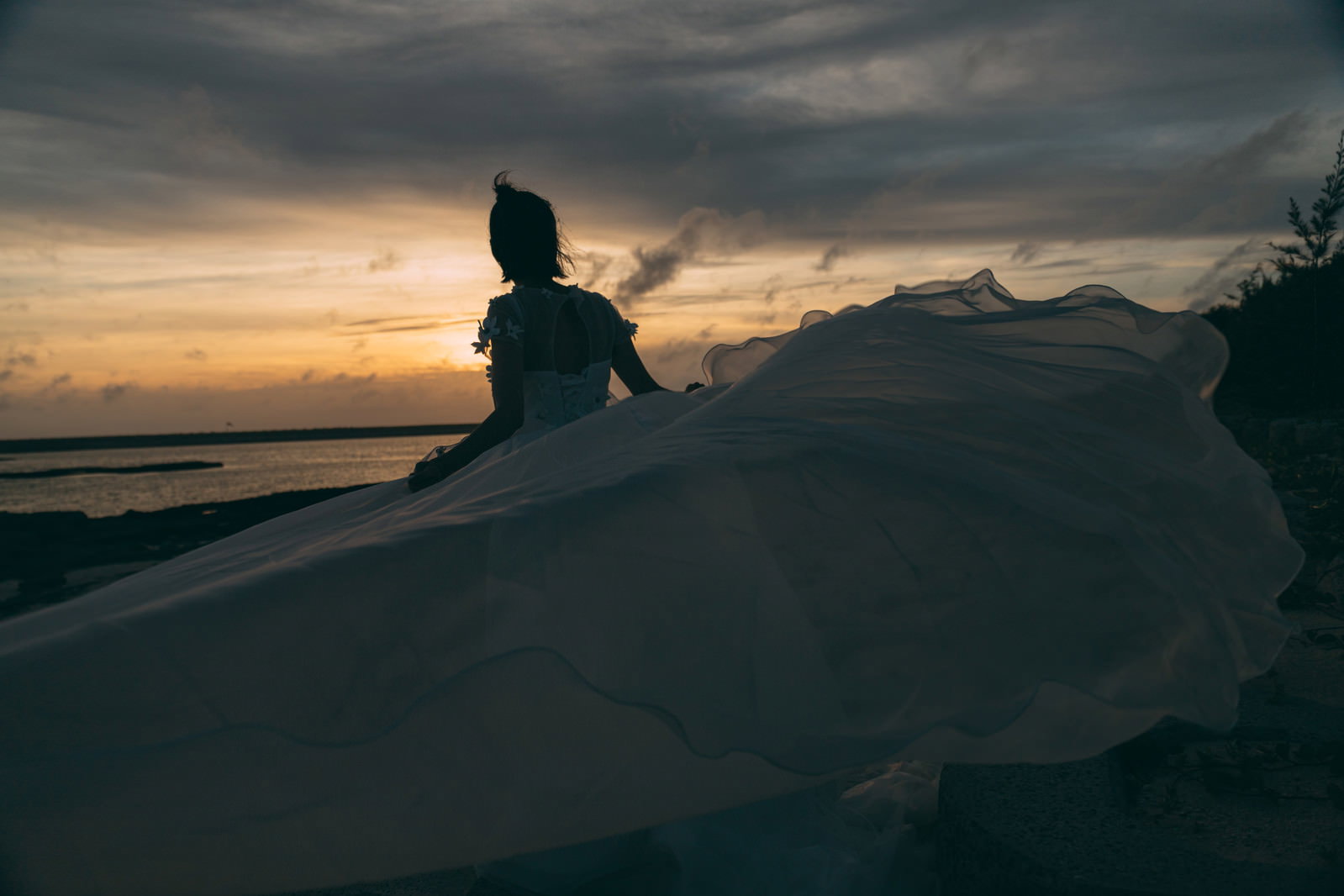 夕焼け空の下、砂浜でウェディングドレスを着た女性のシルエット［モデル：モデルリリース］