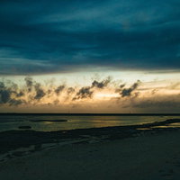 日没に焼ける空と砂浜の海、夕焼けに染まるビーチの風景の写真