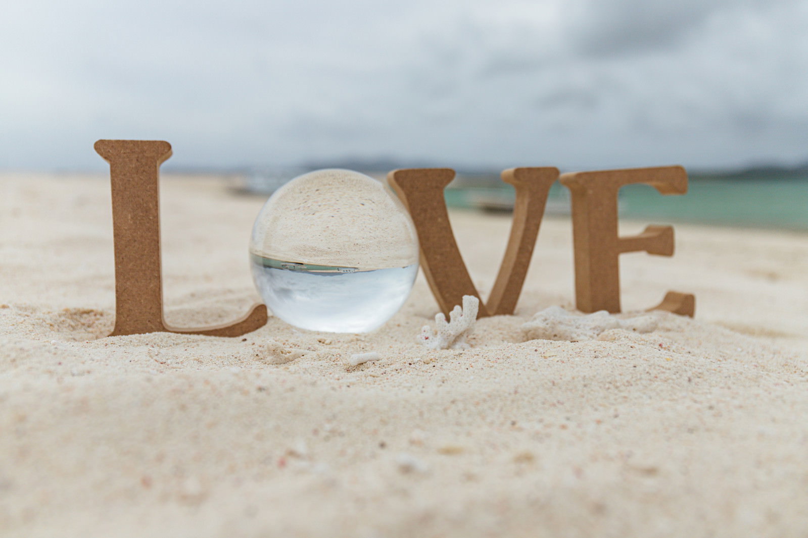 砂浜に置かれた木製のLOVE文字と透明な水晶玉、背景に青い海