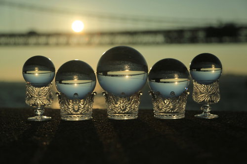 一列に並んだ水晶越しに見る夕日と橋のシルエット