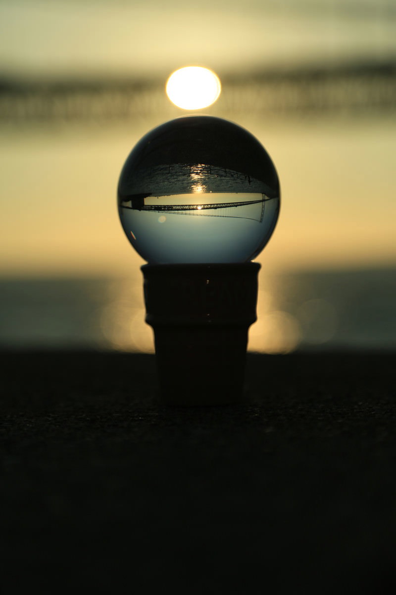 水晶玉に夕日と橋が逆さまに映り込んでいる夕焼け空の風景