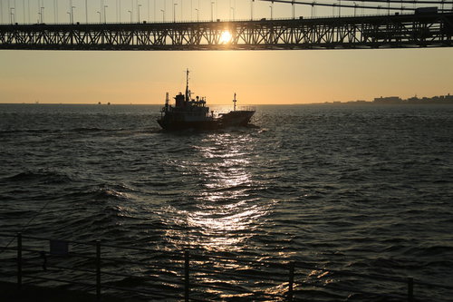 夕焼けに染まる海での小型船と橋のシルエット