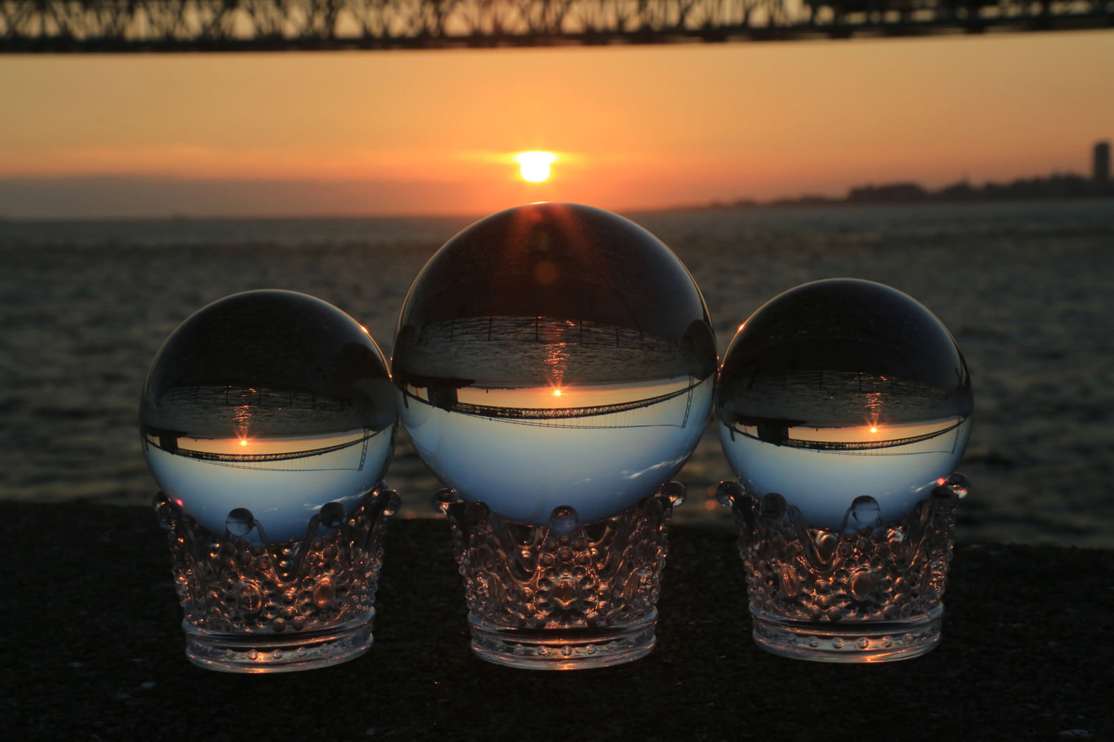 海岸で夕日を背景に3つの水晶玉が並んでいる様子