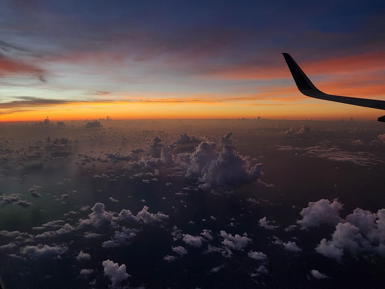 飛行機の翼の先に見える夕焼けで染まった雲海の風景