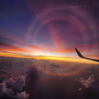 飛行機の窓から見える夕焼けと雲海、翼と地平線のグラデーションの写真