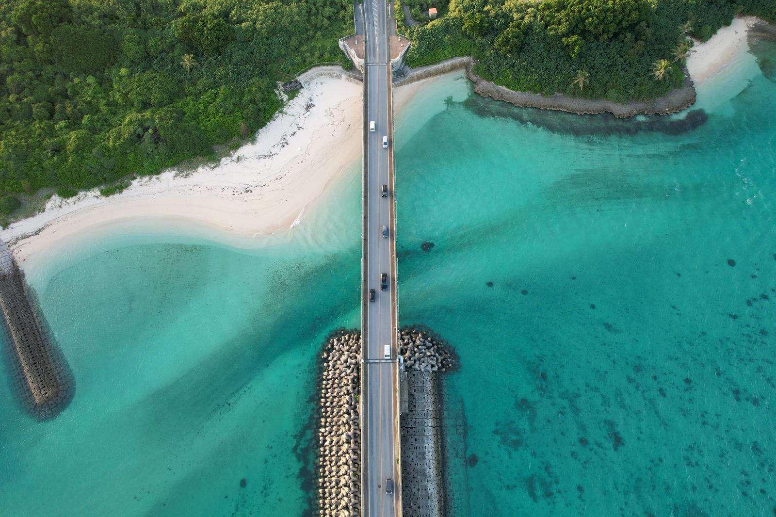 沖縄の透き通ったターコイズブルーの海と砂浜に架かる橋を上空から撮影した写真