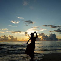 波打ち際で夕焼けを前に佇む女性のシルエットの写真