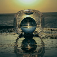 波打ち際に置かれたガラス玉に映る夕陽と海の風景の写真