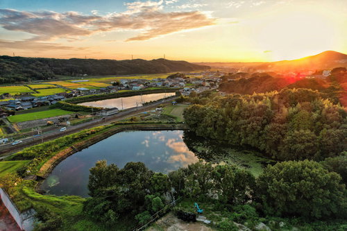 日没迫る夕景と街並み、山々に囲まれた田園の空撮風景