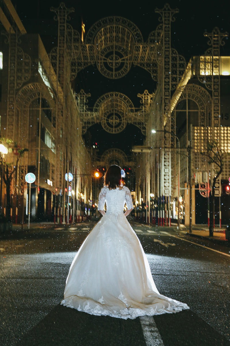 A woman in a white dress standing on a cobblestone street with the unlit Kobe Luminarie decorations in the background