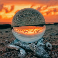 ガラス玉から見る燃えるような夕焼けと海岸の写真