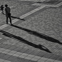石畳の広場を歩くお出かけ中の家族連れと伸びる影の写真