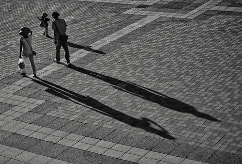 石畳の広場を歩くお出かけ中の家族連れと伸びる影