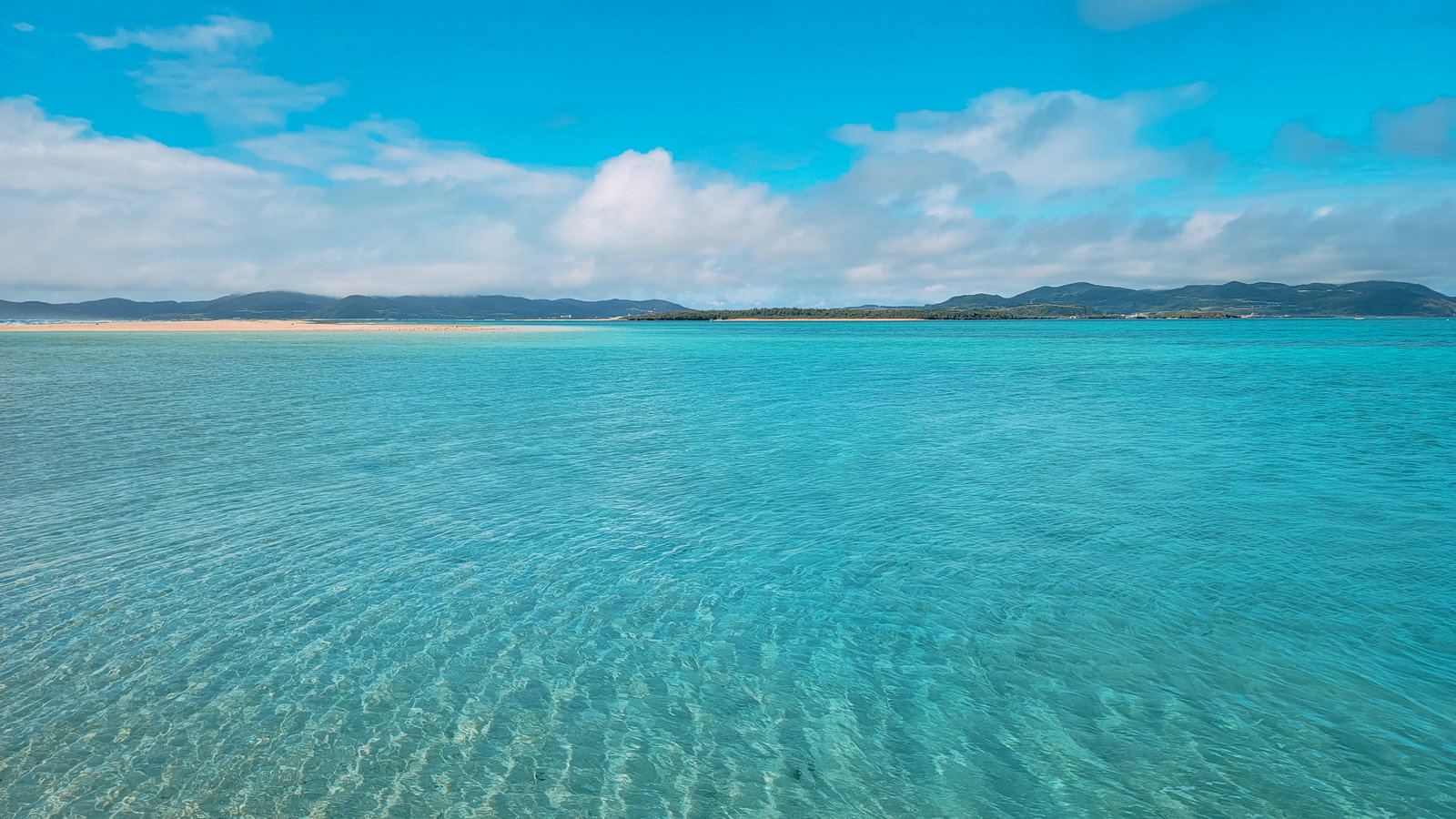 透明度の高いエメラルドグリーンの海と青空が広がる南国リゾートの風景