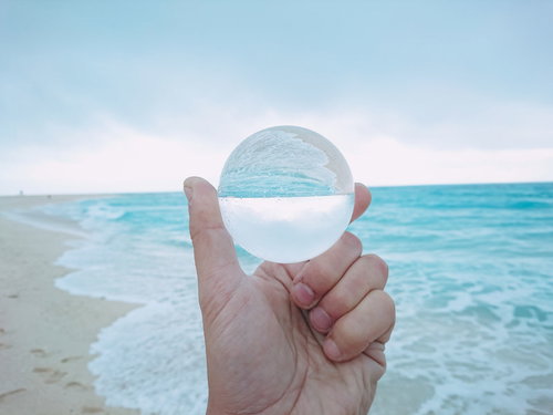 波打ち際で手に持ったガラス玉と海の景色
