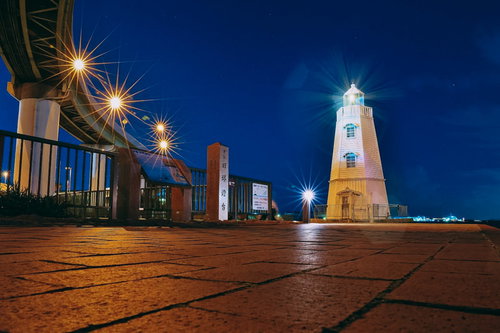 夜の旧堺燈台にさす光芒と夜景、歴史的建造物のライトアップ