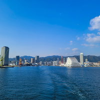 海面に残る船跡と遠ざかる埠頭、対岸の高層ビル群の写真