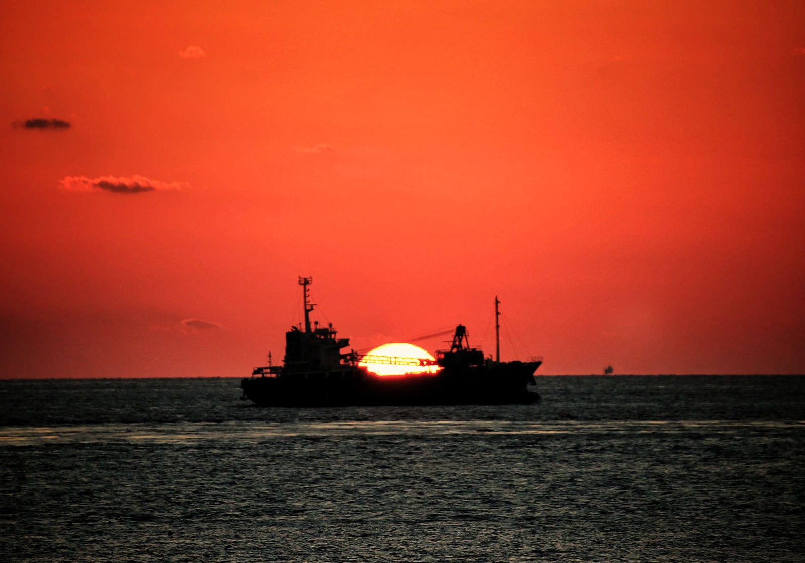 オレンジ色の夕焼け空と水平線に浮かぶ貨物船のシルエット