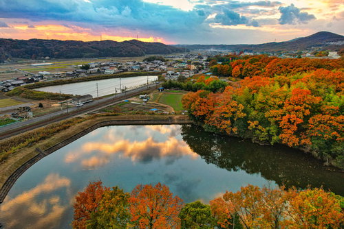 秋の夕暮れにオレンジ色に染まる紅葉と川面の水鏡