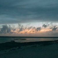 雲間に見える焼けた空と朝焼けの浜辺、波打つ砂浜の写真