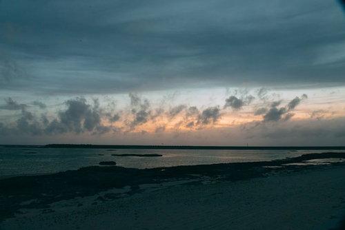 雲間に見える焼けた空と朝焼けの浜辺、波打つ砂浜