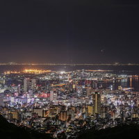 遠くに見える都市の夜景と港の灯り、水面に映る夜間の都市風景の写真